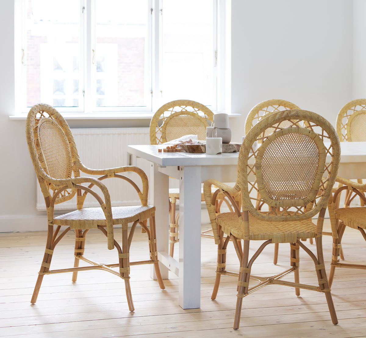 Dette er et livsstilsbillede af Romantica Spisebordsstol i natural rattan. Samlet omkring et hvidt spisebord i et lyst skandinavisk rum.