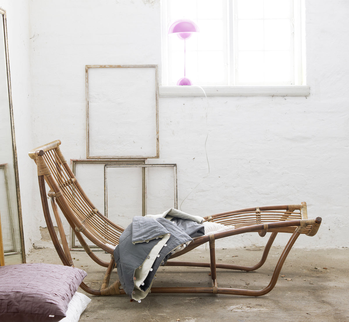 Dette er et livsstilsbillede af Michelangelo Daybed i antique rattan. Stylet med linnedplaider i et hvidt studie med vintage-rammer.