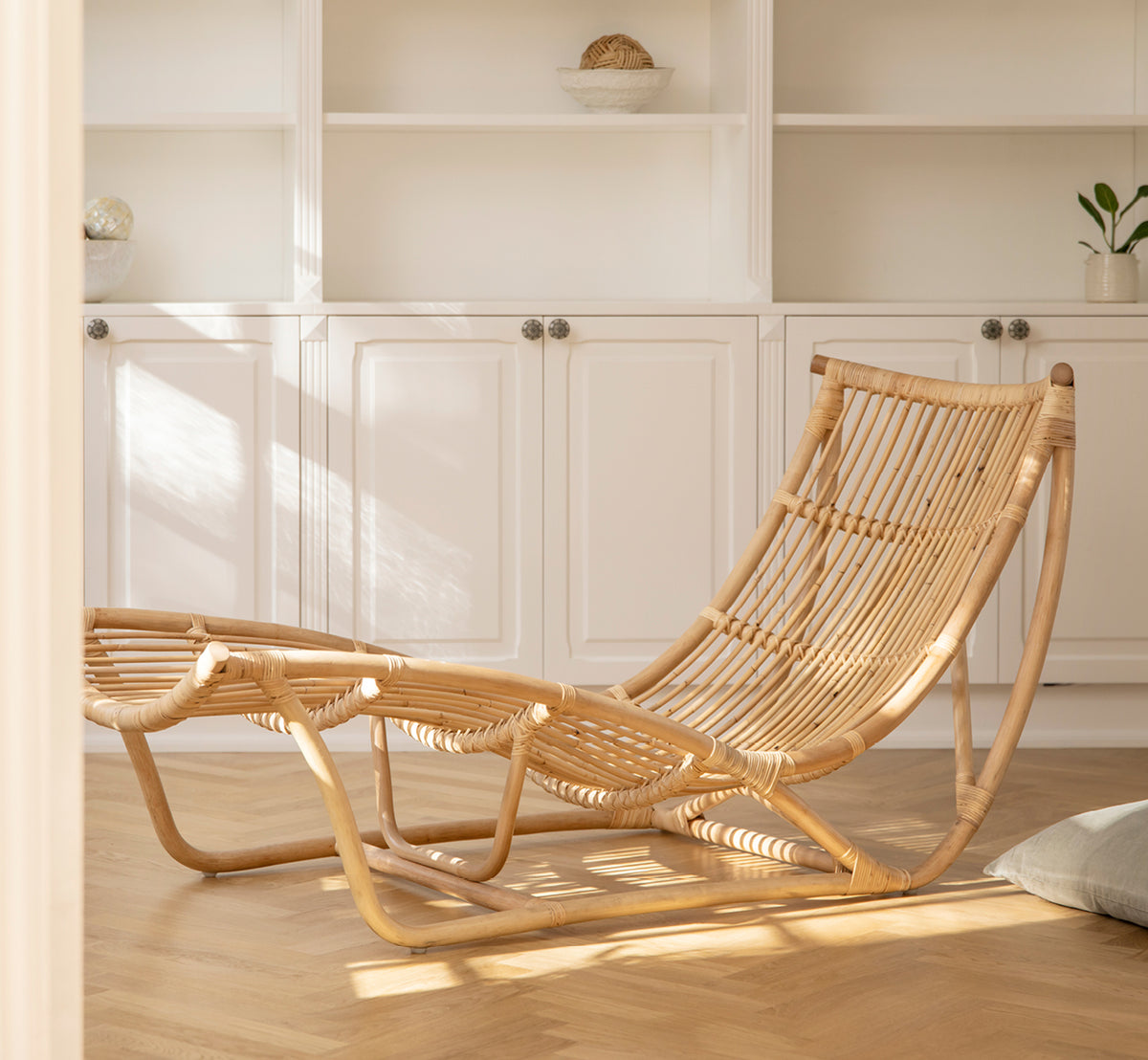 Dette er et livsstilsbillede af Michelangelo Daybed i natural rattan. Placeret i et lyst hvidt rum med betongulv og lyserød lampe.