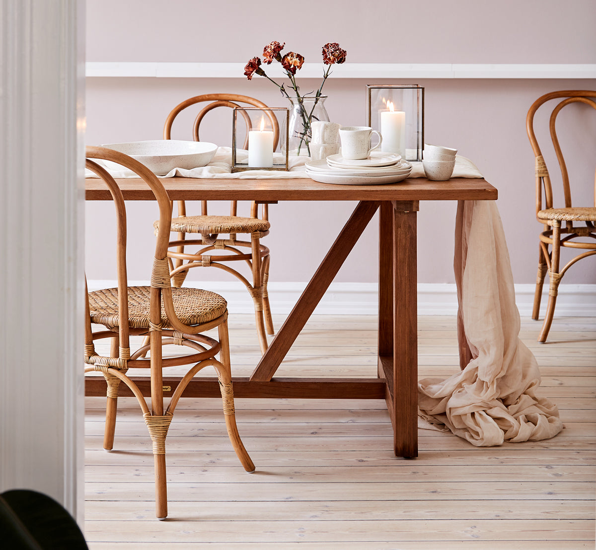 Dette er et livsstilsbillede af Lulu Spisebordsstol i antique rattan. Stylet ved et teakspisebord med stearinlys og linned i et varmt interiør.