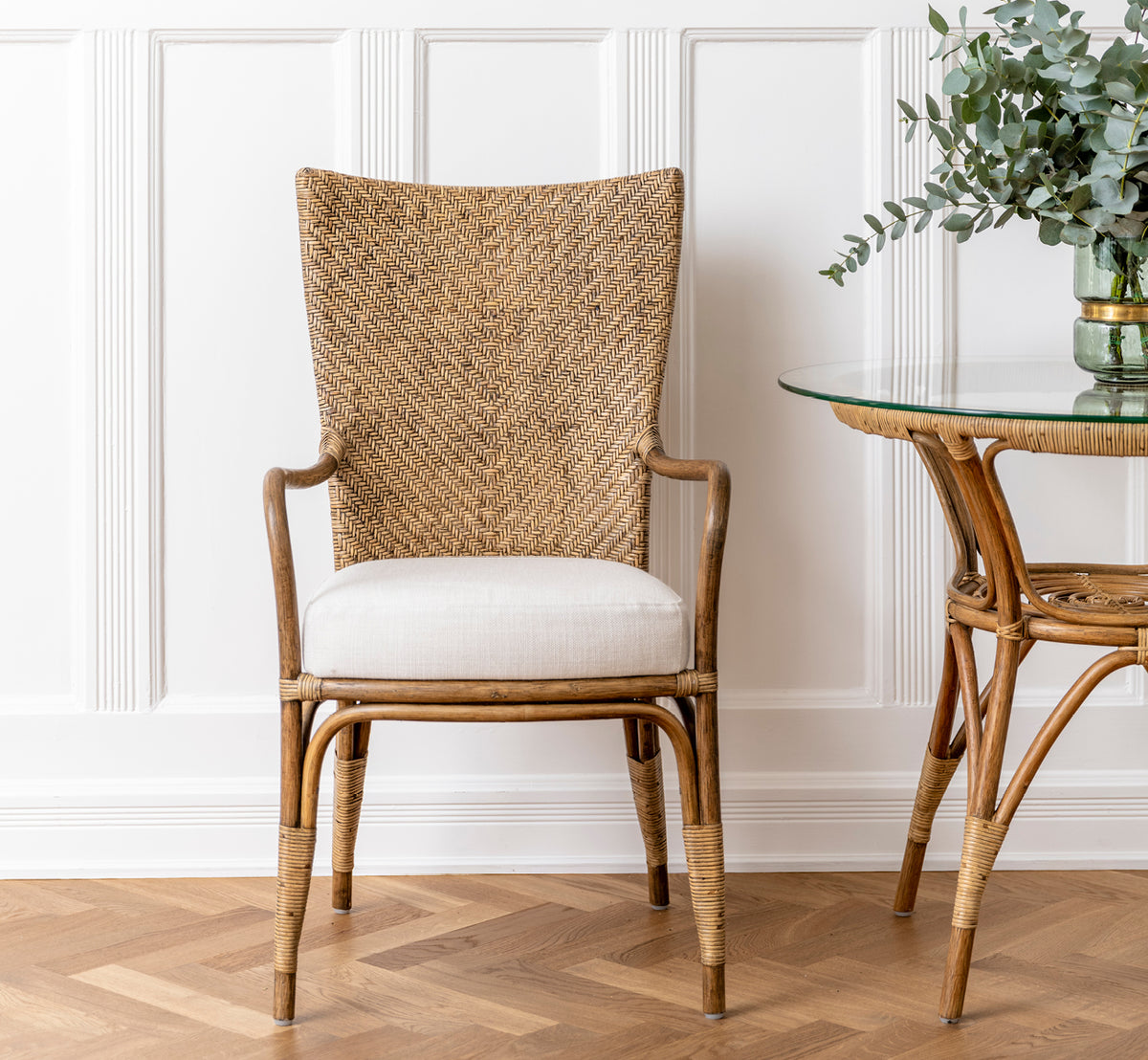 Dette er et livsstilsbillede af Melody Dining Armchair i antique rattan. Placeret ved et hvidt spisebord i et lyst skandinavisk rum.