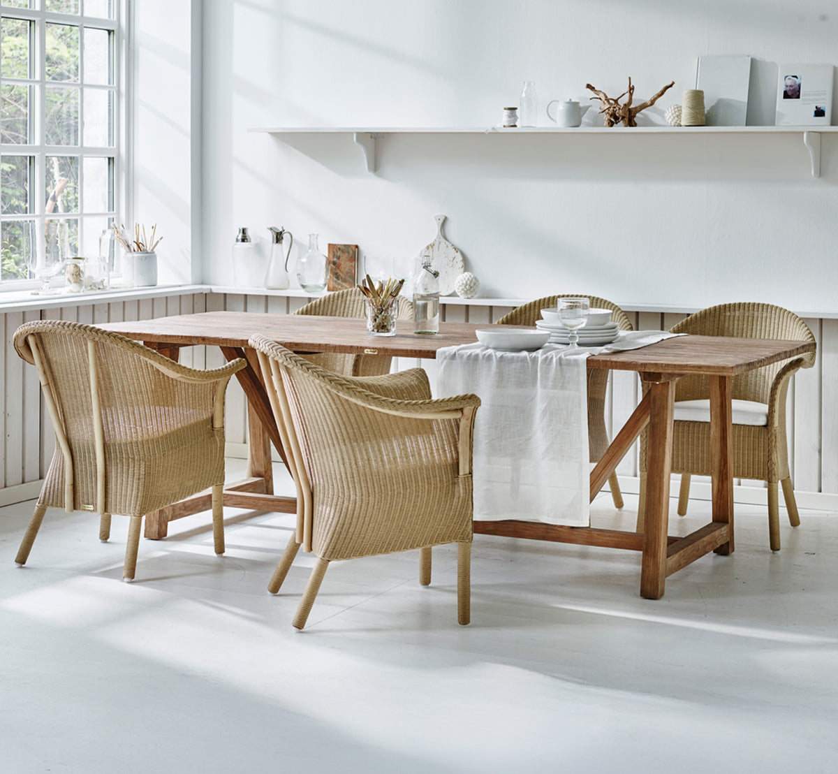 Dette er et livsstilsbillede af Classic Spisebordsstol i natural Loom Rattan Frame, i et lyst interiør med hvide panelvægge og sildebensgulv.