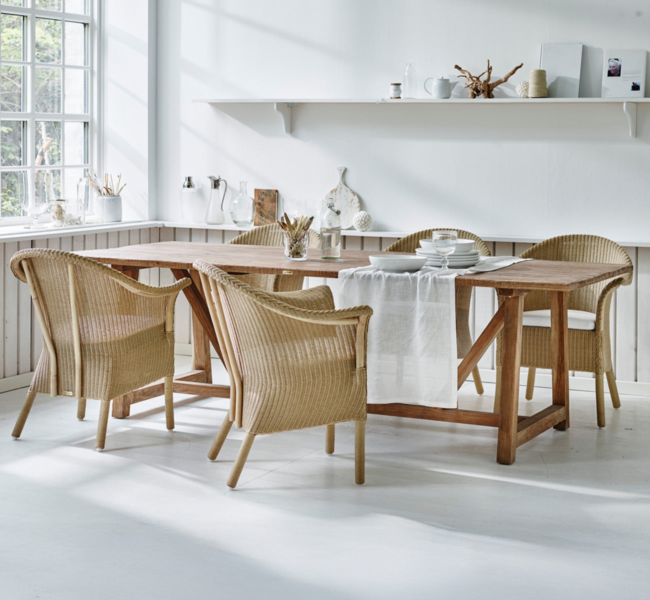 Dette er et livsstilsbillede af Classic Spisebordsstol i natural Loom Rattan Frame, i et lyst interiør med hvide panelvægge og sildebensgulv.
