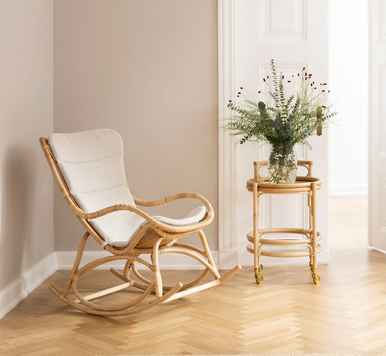 Dette er et livsstilsbillede af Monet Rocking Chair i natural rattan. I et rum med rosa vægge, sildebensgulv og eucalyptus.