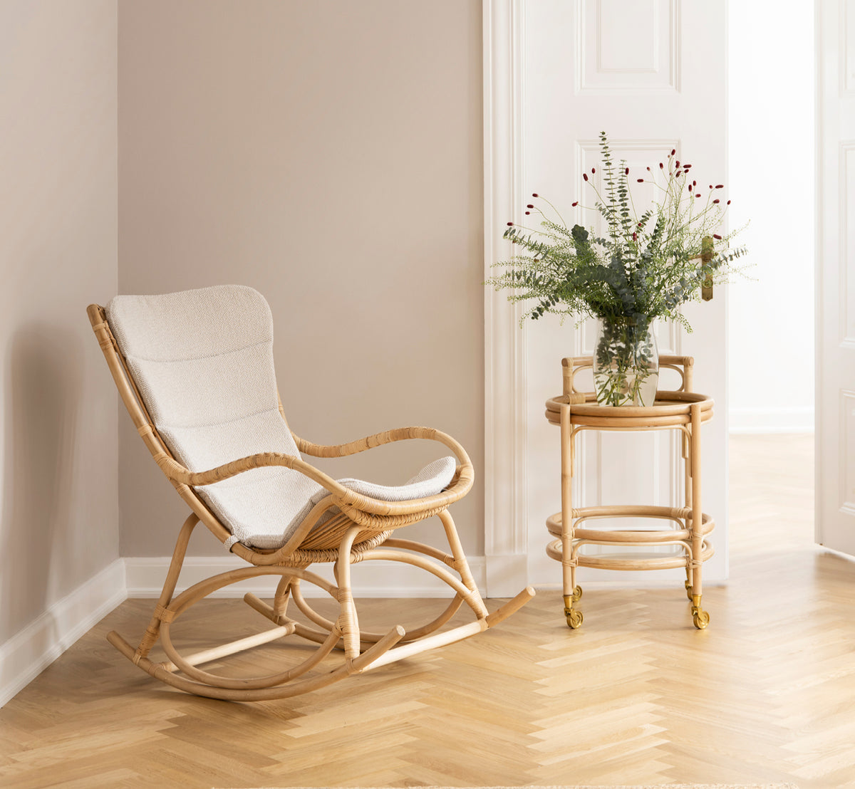 Dette er et livsstilsbillede af Monet Rocking Chair i natural rattan. I et rum med rosa vægge, sildebensgulv og eucalyptus.