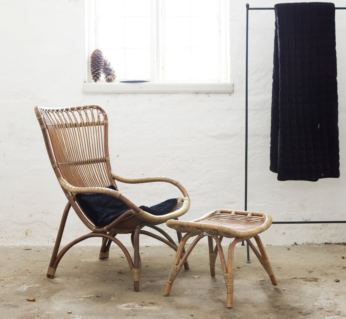 Dette er et livsstilsbillede af Monet Lounge Chair i antique rattan. Med fodskammel og sidebord i en mørk rustik ladescene.