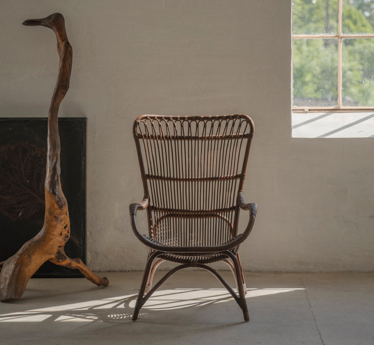 Dette er et livsstilsbillede af Monet Lænestol i brown rattan. Ved drivtømmer i et rustikt rum med betongulv.