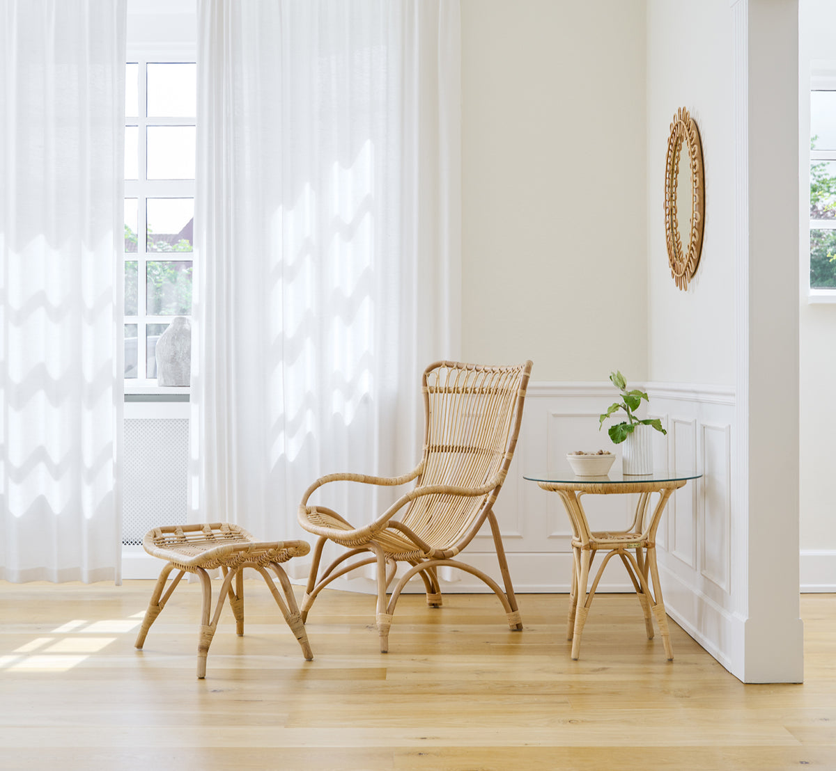 Dette er et livsstilsbillede af Monet Lounge Chair i natural rattan. Med fodskammel i et lyst rum med egegulv og lette gardiner.