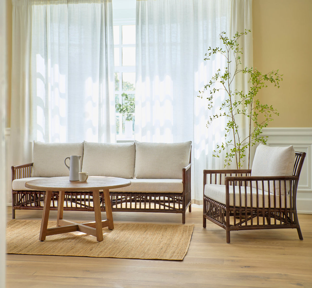 Dette er et livsstilsbillede af Caroline Sofa i brown rattan. Med lænestol og teak sofabord på et jutetæppe.
