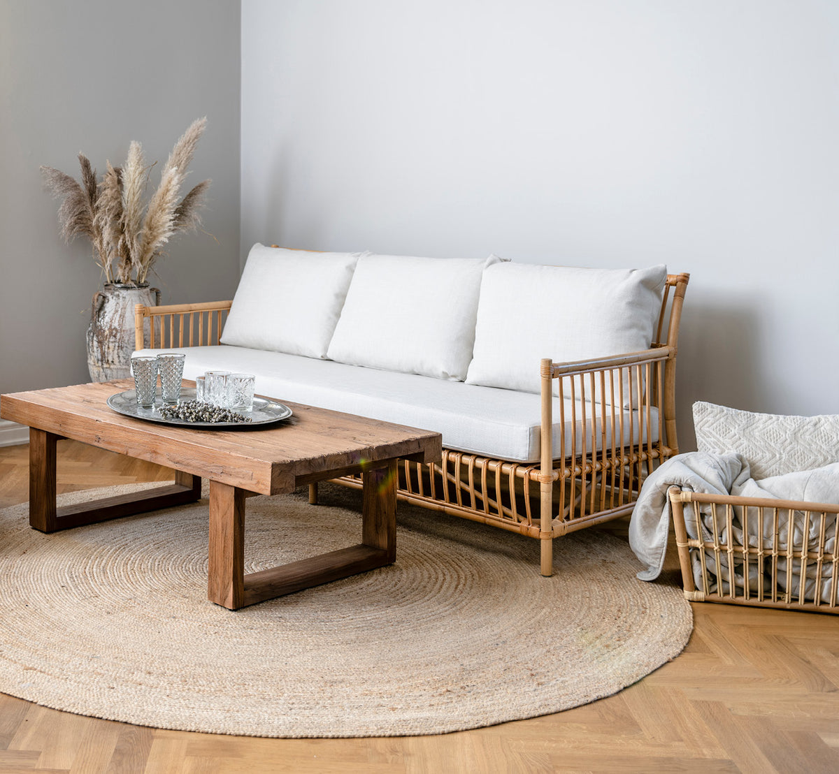 Dette er et livsstilsbillede af Caroline Sofa i natural rattan, i et lyst interiør med hvide panelvægge og sildebensgulv.