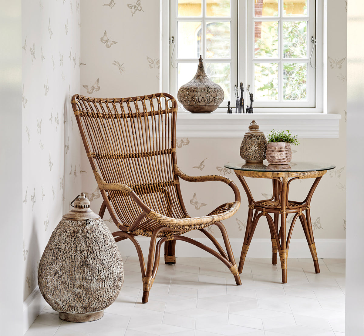 Dette er et livsstilsbillede af Tony Sidebord i antique rattan. Opstillet i et sommerfugle-tapet-hjørne med lanterne og dekoration.