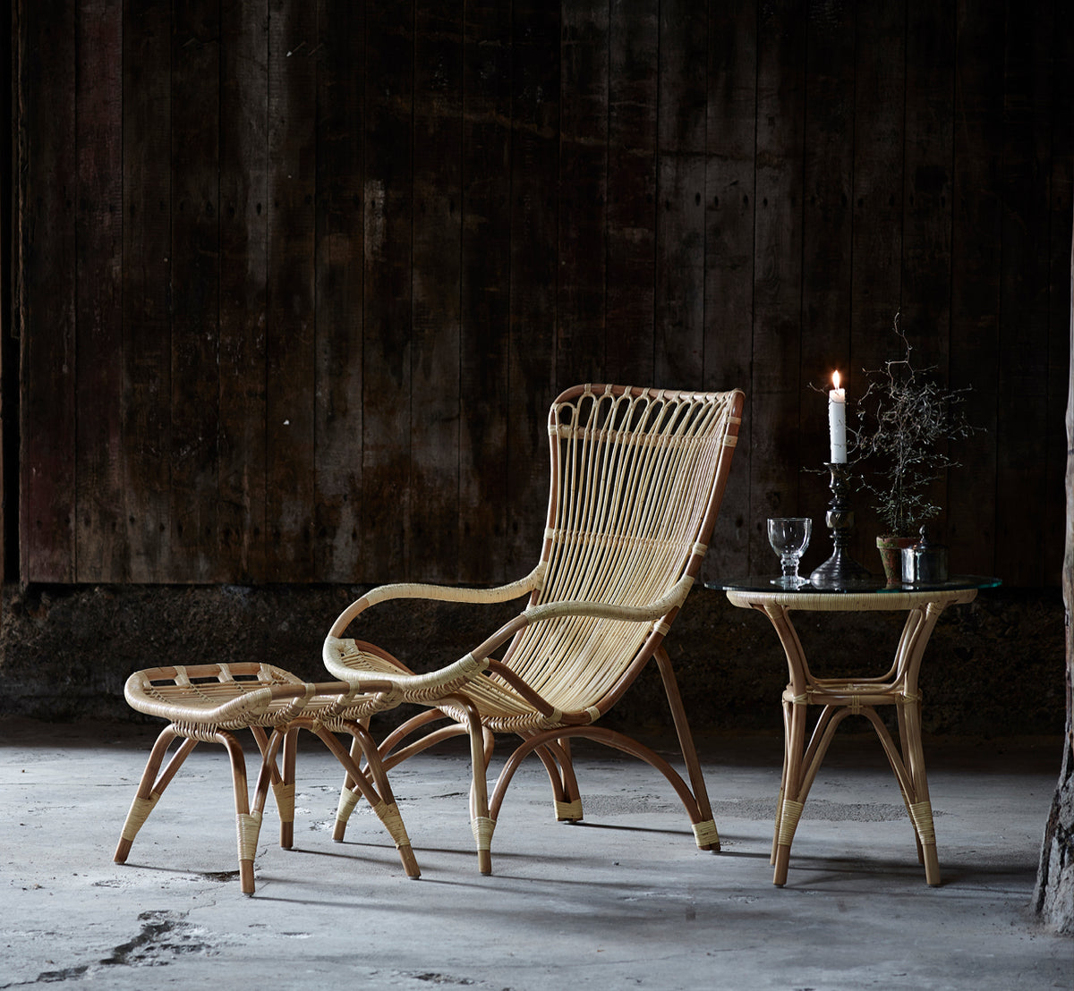 Dette er et livsstilsbillede af Tony Sidebord i natural rattan. Paired with a high-back lounge chair against a dark wood wall.