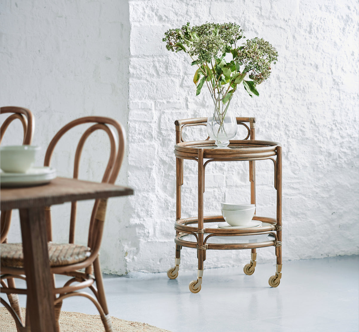 Dette er et livsstilsbillede af Romeo Rullebord i antique rattan. Stylet med hortensiaer og keramik mod en hvid murstensvæg.