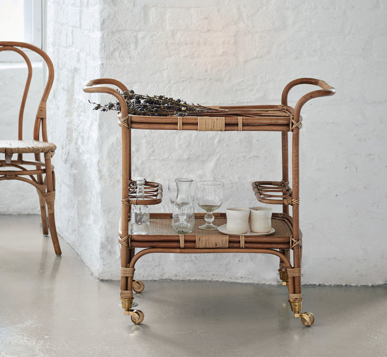 Dette er et livsstilsbillede af Carlo Trolley i antique Rattan, i et lyst hvidt interiør med lambrisering og et rattanspejl på væggen.