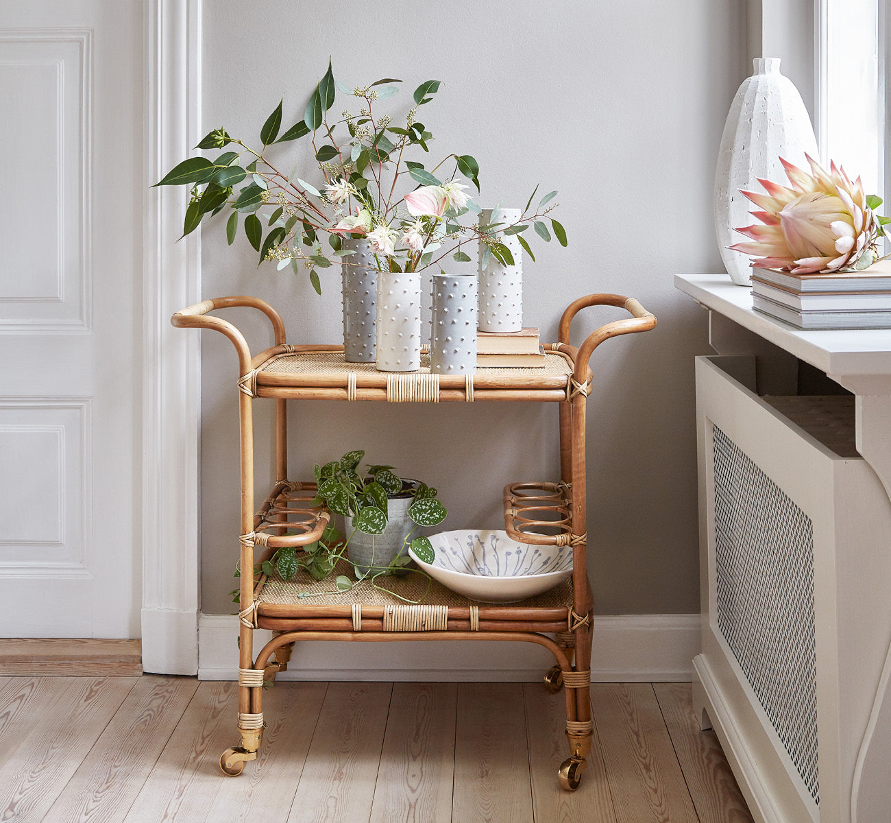 Dette er et livsstilsbillede af Carlo Trolley i antique Rattan, i et lyst hvidt interiør med lambrisering og et rattanspejl på væggen.