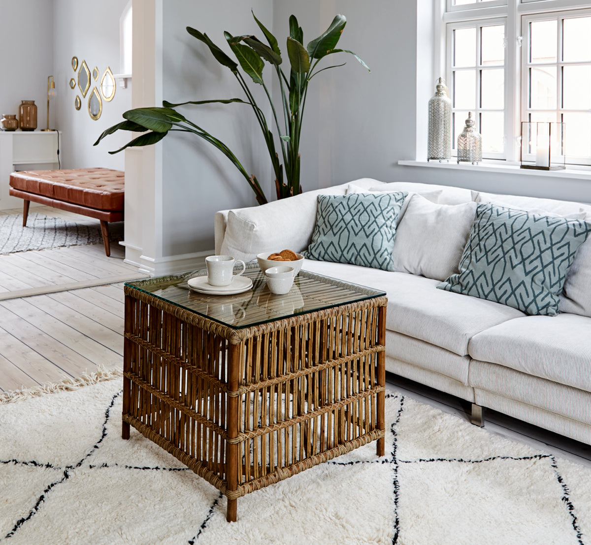 Dette er et livsstilsbillede af Donatello Sidebord i antique rattan, i et lyst interiør med hvide panelvægge og sildebensgulv.