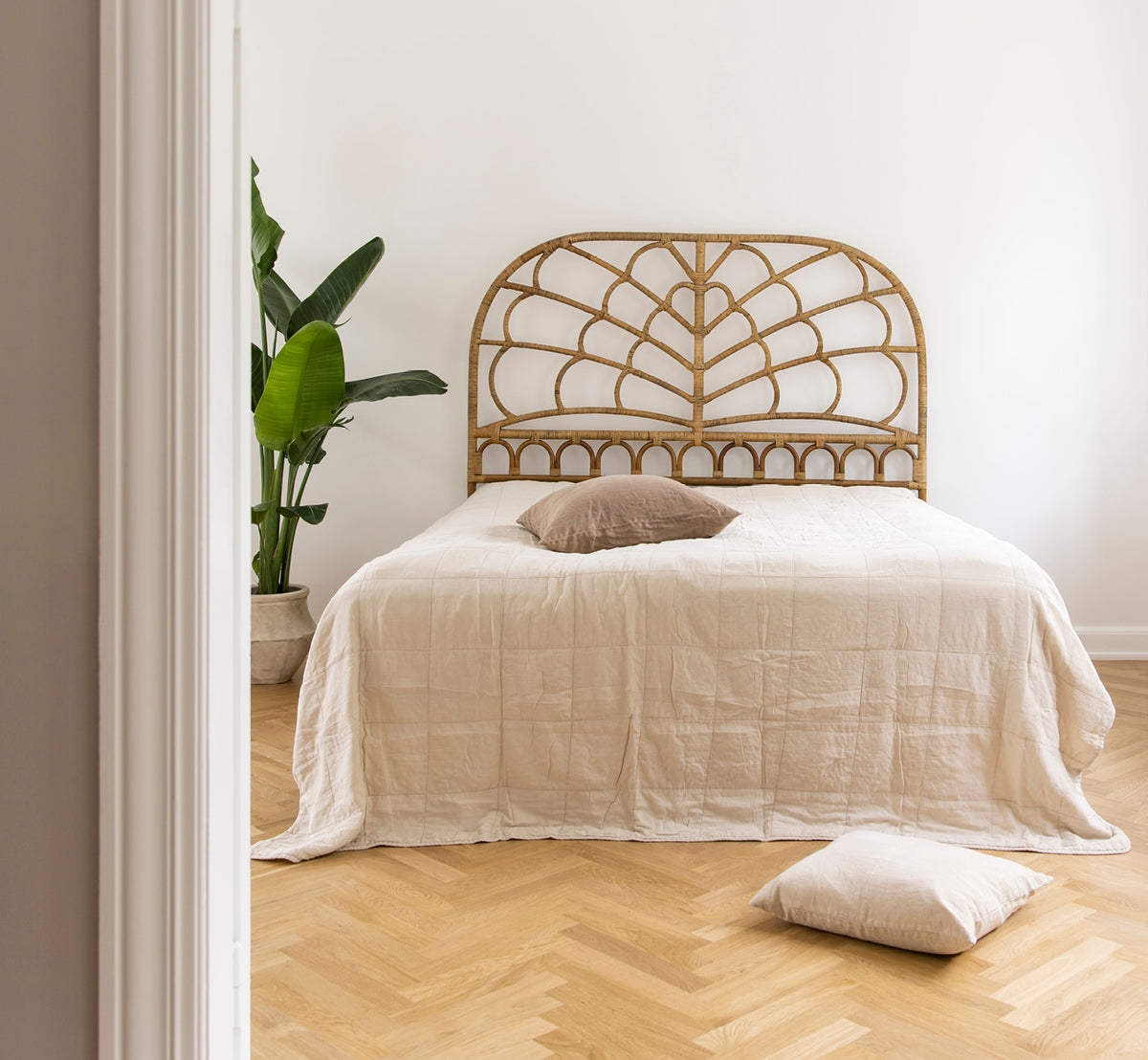 Dette er et livsstilsbillede af Celia Sengegavl i antique rattan, i et roligt lyst soveværelse med neutralt linned og sildebensgulv.