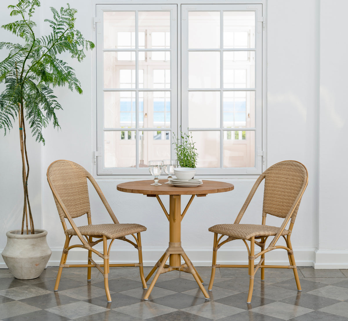 Dette er et livsstilsbillede af Sofie Exterior Dining Chair i almond aluminium frame natural ArtFibre. Omkring et udendørs teakbord.