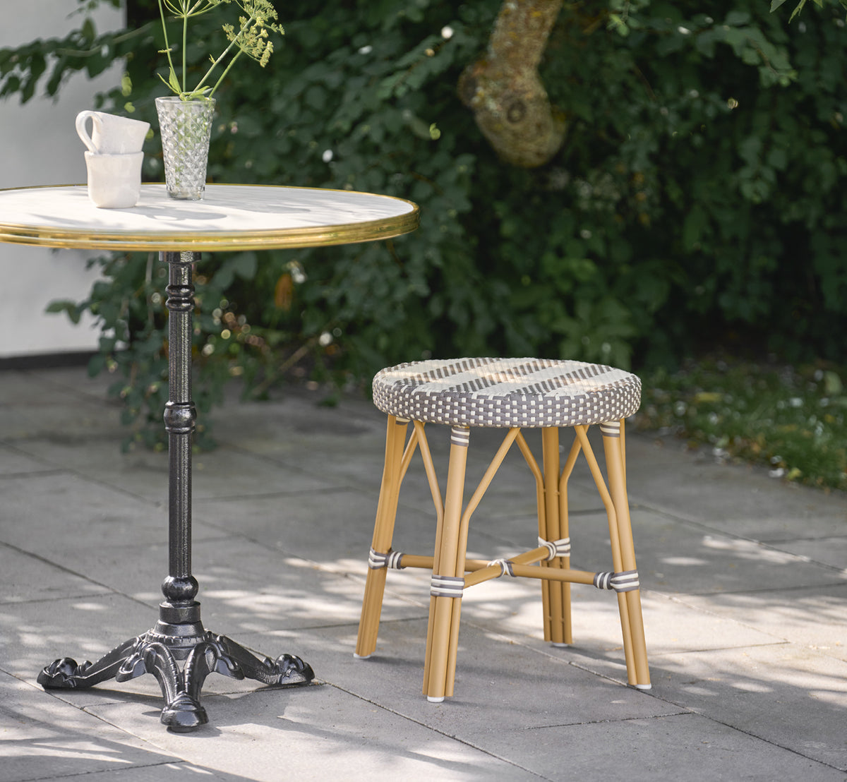 Dette er et livsstilsbillede af Simone Udendørs skammel i almond aluminium frame striped cappuccino ivory artfibre. Stylet i et lyst interiør.