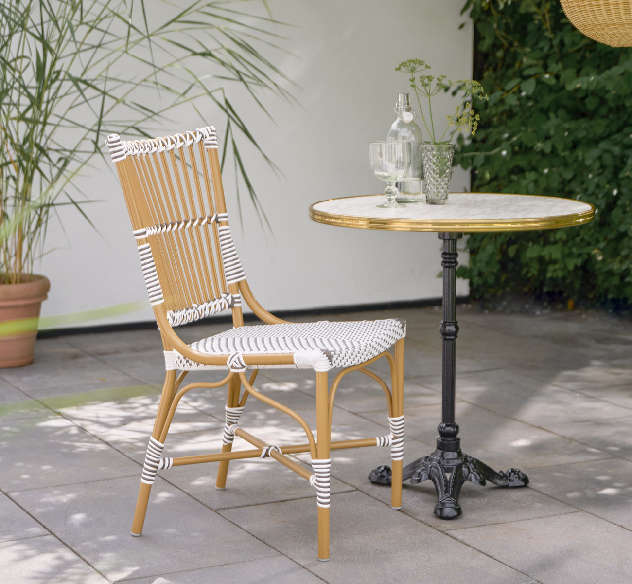 Dette er et livsstilsbillede af Monique Exterior Dining Chair i white w cappuccino dot ArtFibre. På en solrig terrasse med palmer.