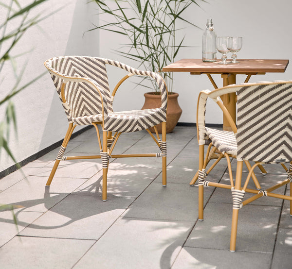 Dette er et livsstilsbillede af Madeleine Udendørs spisebordsstol i almond aluminum frame chevron cappuccino ivory ArtFibre. Solrig terrasse med teakbord.