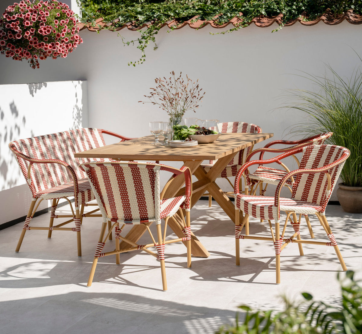 Dette er et livsstilsbillede af Madeleine Udendørs bænk i almond aluminum frame striped ivory burgundy. Med teakbord på en solrig terrasse.