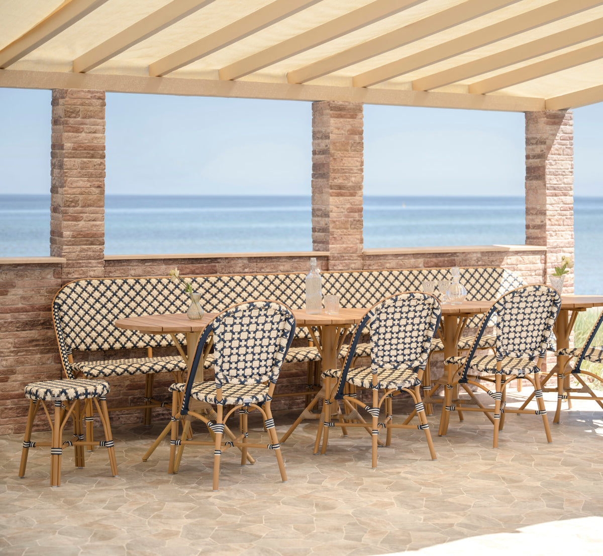 Dette er et livsstilsbillede af Sofie Udendørs 6-personers bænk i almond aluminium frame starweave ivory navy blue cappuccino artfibre. Ved havet.