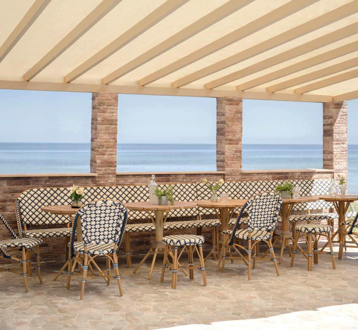 Dette er et livsstilsbillede af Sofie Udendørs 8-personers bænk i almond aluminium frame starweave ivory navy blue cappuccino artfibre. Ved havet.