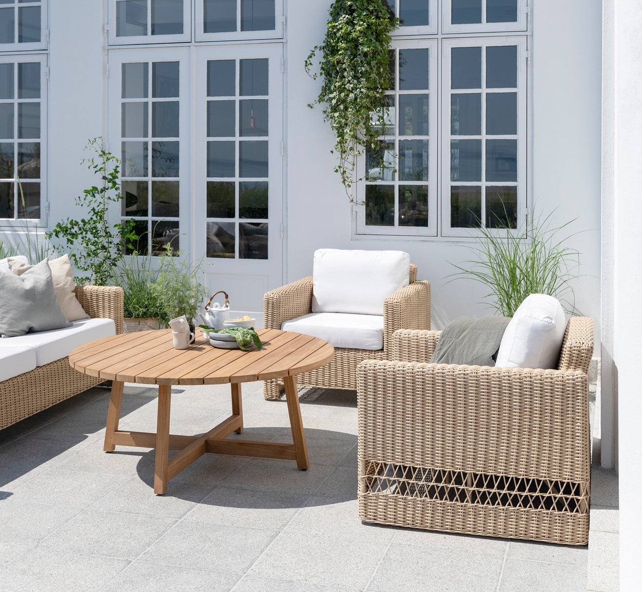 Dette er et livsstilsbillede af Carrie Lænestol i natural ArtFibre Aluminium, på en soldrenkt kystterrasse med havudsigt og hvid pergola.