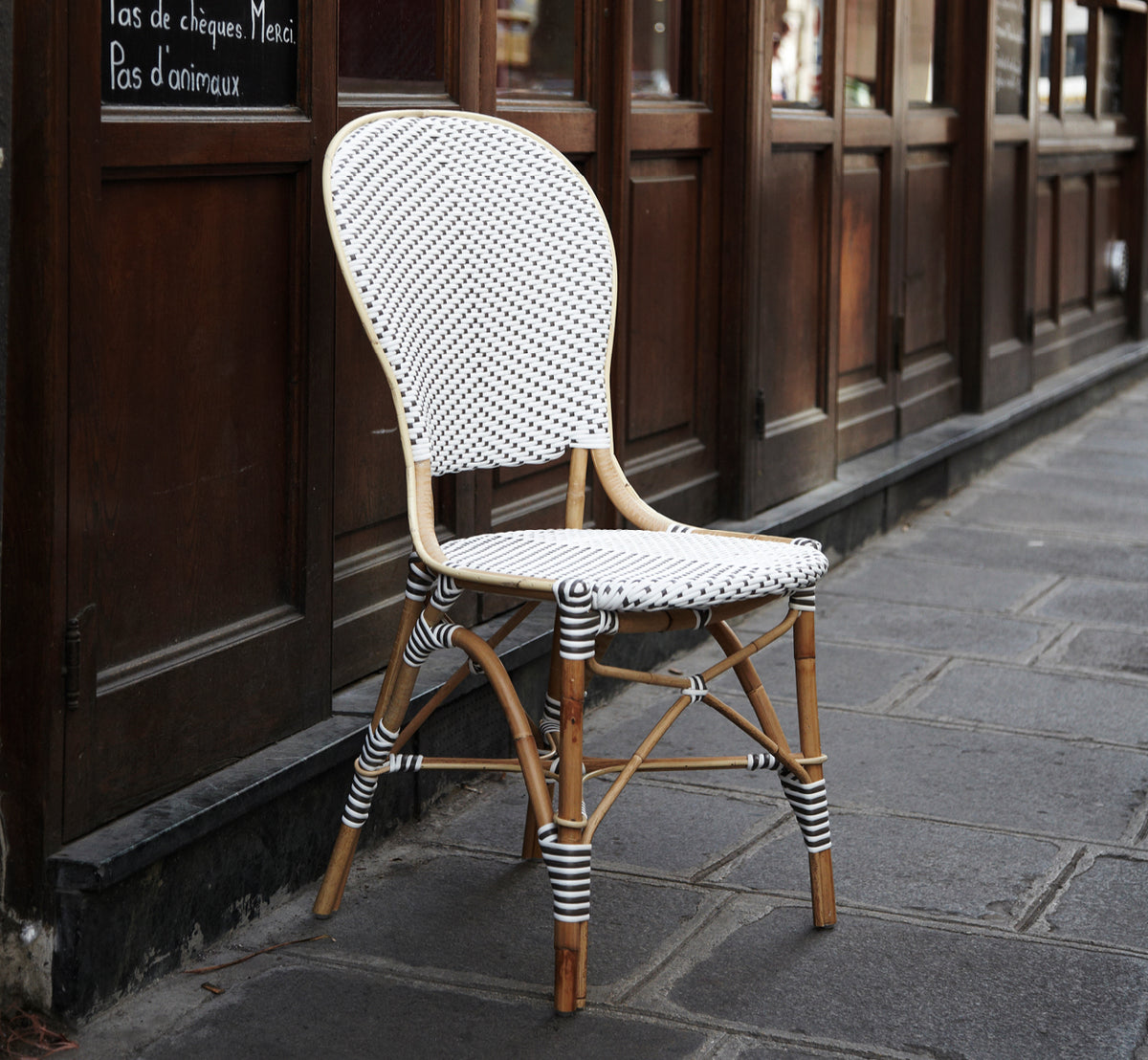 Dette er et livsstilsbillede af Isabell i white w cappuccino dot ArtFibre Skin on Rattan frame, på en lys kystterrasse med havudsigt og tropisk grønt.