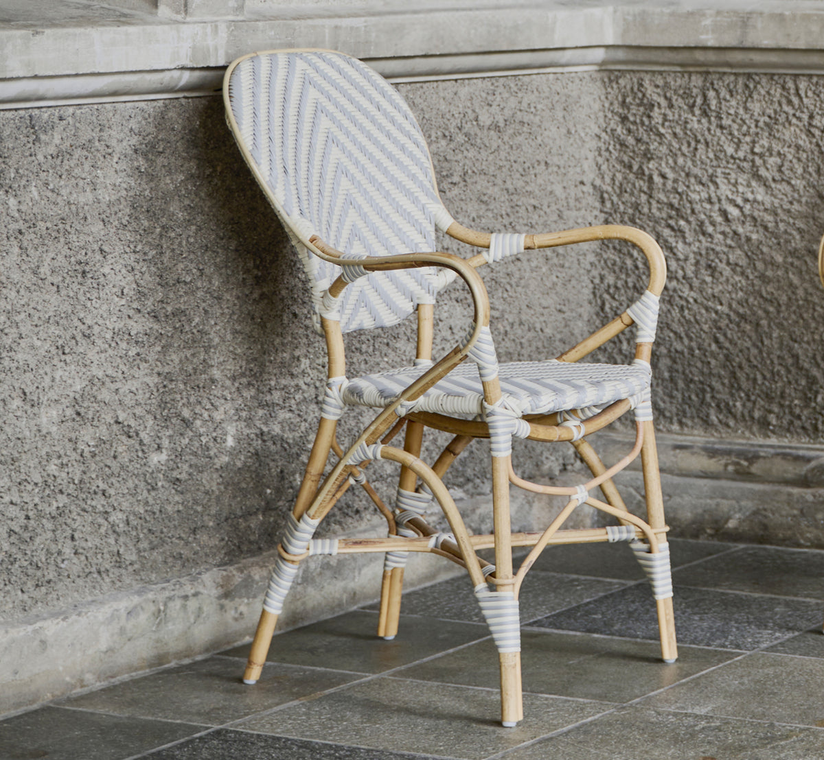 Dette er et livsstilsbillede af Isabell Spisestuelænestol i chevron Grey Ivory ArtFibre Skin on Rattan frame, i et lyst spiseområde med store vinduer.