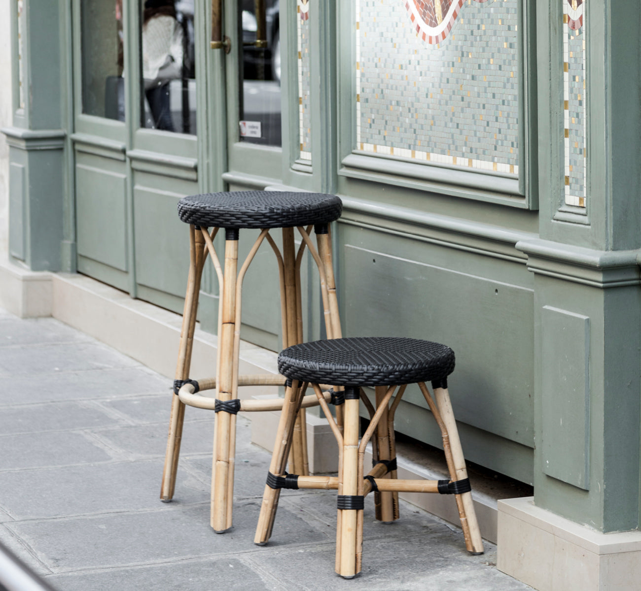 Dette er et livsstilsbillede af Simone Skammel i black ArtFibre Skin on Rattan frame. Placeret foran en grøn parisisk caféfacade.