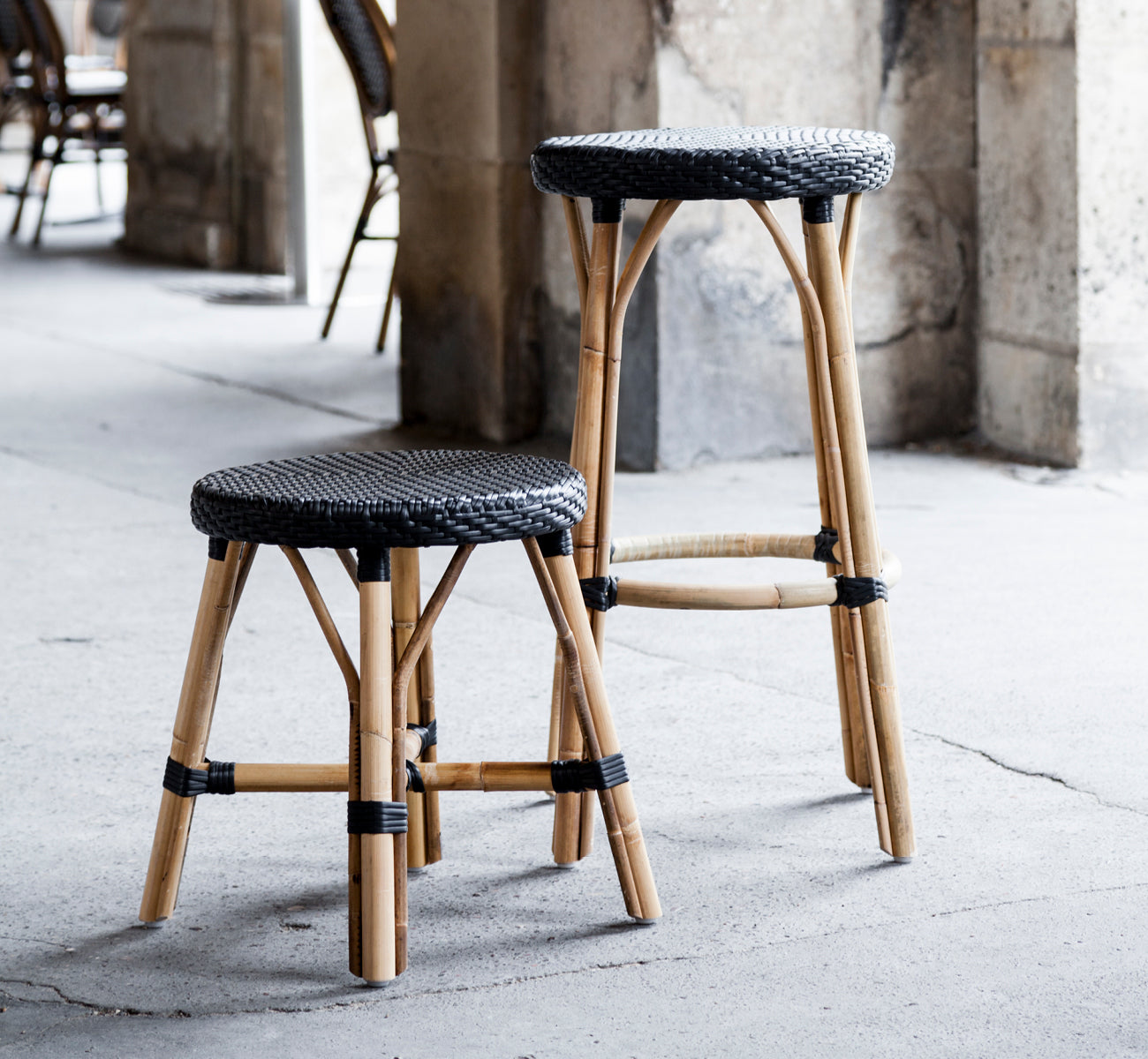 Dette er et livsstilsbillede af Simone Skammel i black ArtFibre Skin on Rattan frame. Placeret ved stensøjler i et cafémiljø.