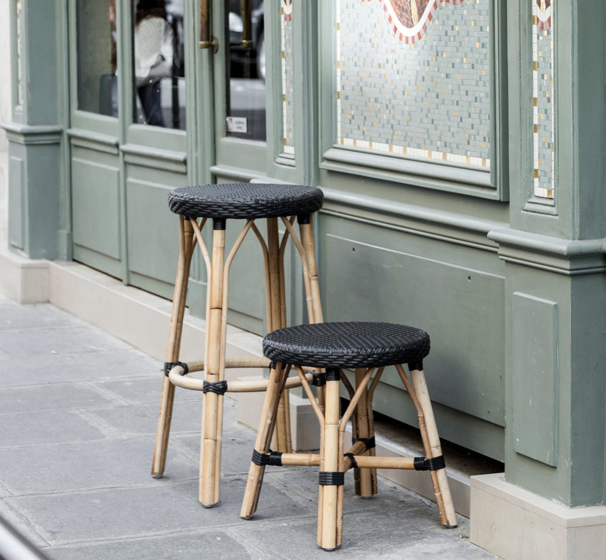 Dette er et livsstilsbillede af Simone Skammel i black ArtFibre Skin on Rattan frame. Placeret foran en grøn parisisk caféfacade.