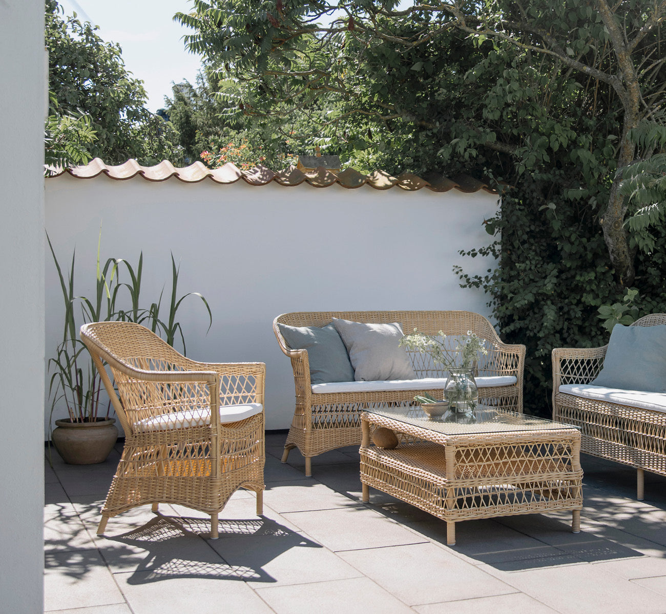 Dette er et livsstilsbillede af Charlot Stol i natural ArtFibre Aluminium, på en soldrenkt kystterrasse med havudsigt og en hvid pergola.