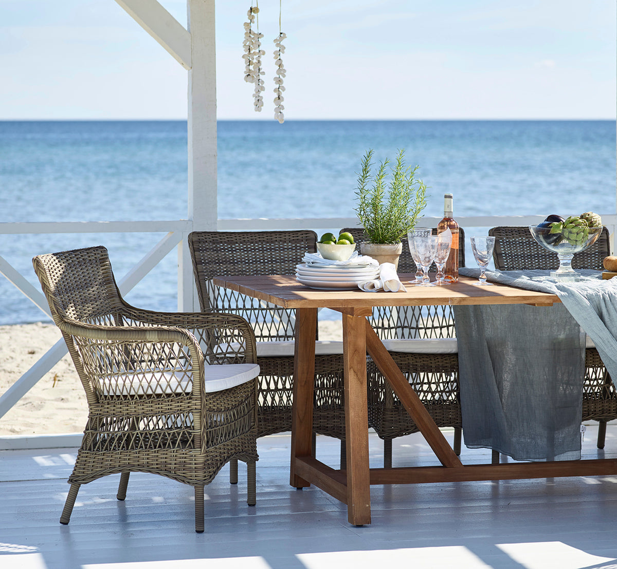 Dette er et livsstilsbillede af Marie Exterior Armchair i antique grey artfibre aluminium. Omkring et teakbord i en strandpavillon.
