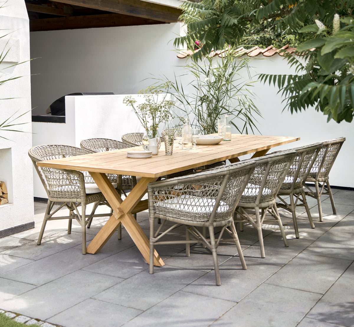 Dette er et livsstilsbillede af Emma Udendørs Spisebordsstol i antique Grey ArtFibre Aluminium, på en lys kystterrasse med sivtag og havudsigt.