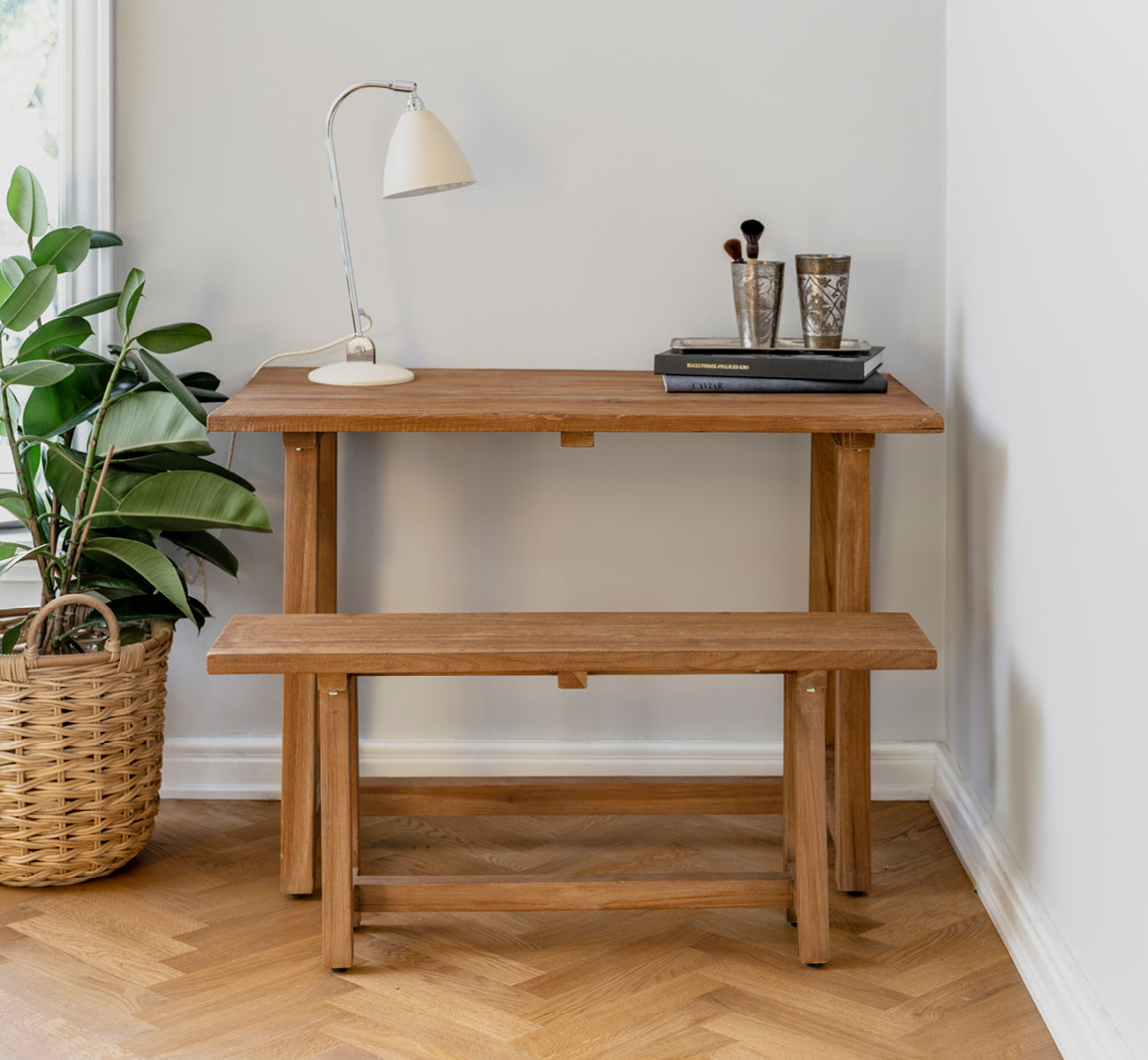 Dette er et livsstilsbillede af Lucas Teak Bænk i teak indoor. Kombineret med et teakskrivebord, lampe og bøger i et hyggeligt hjørne på sildebensgulv.
