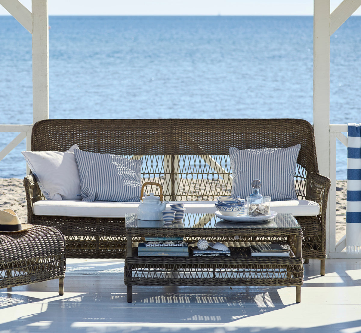 Dette er et livsstilsbillede af Dawn Sofa i antique Grey ArtFibre Aluminium, på en kystterrasse med hvidt trædæk og havudsigt.