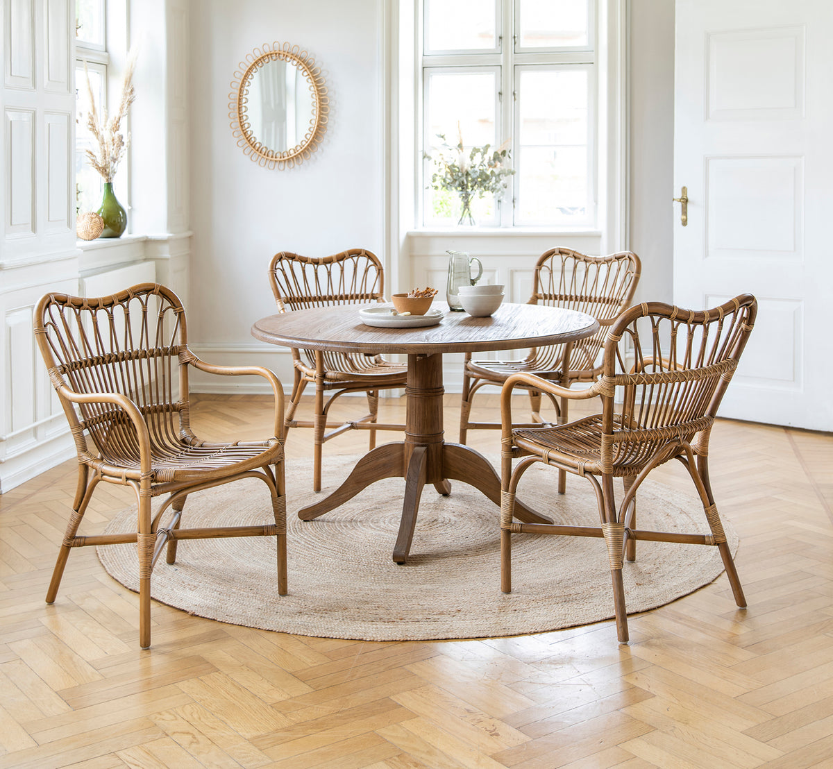 Dette er et livsstilsbillede af Michel Teak Dining Table i teak indoor. Med Rossini-stole på et jutetæppe i en lys hvid loft.