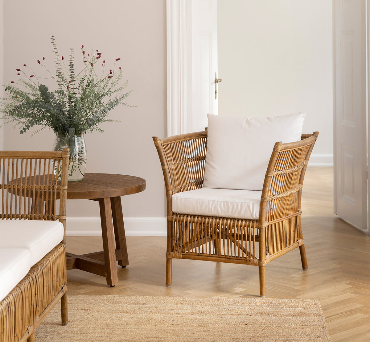 Dette er et livsstilsbillede af Aksel Sofabord i teak indoor, i et lyst interiør med sildebensgulv og rattanstole.