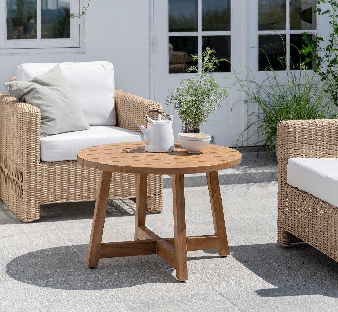 Dette er et livsstilsbillede af Victor Teak Lounge Table Ø75 cm i teak outdoor. Opstillet på en strandterrasse mellem daybeds med stribede puder.