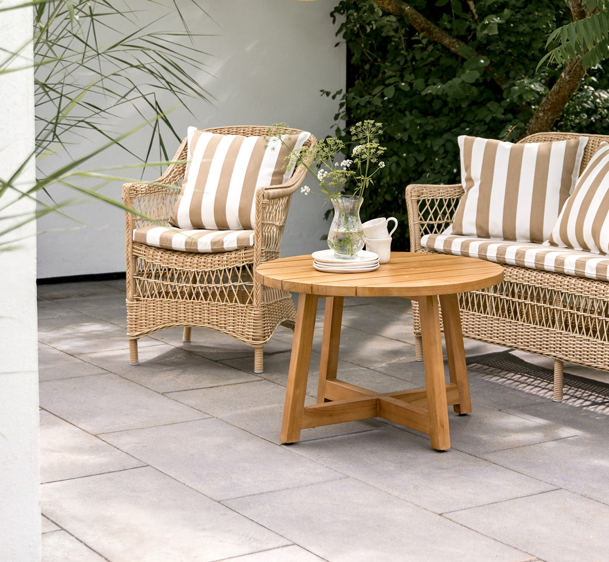 Dette er et livsstilsbillede af Victor Teak Lounge Table Ø75 cm i teak outdoor. Opstillet på en strandterrasse mellem daybeds med stribede puder.