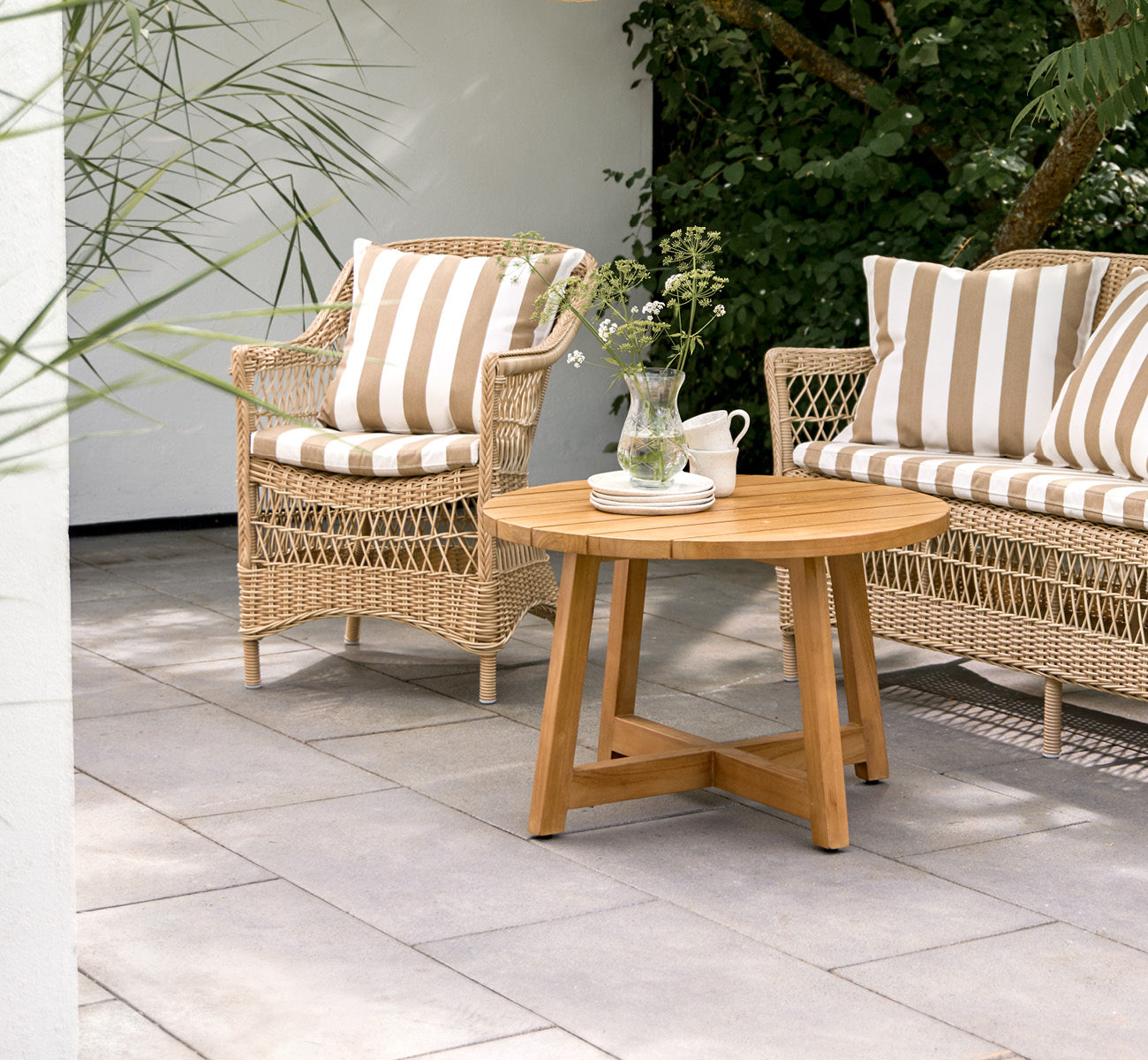 Dette er et livsstilsbillede af Victor Teak Lounge Table Ø75 cm i teak outdoor. Opstillet på en strandterrasse mellem daybeds med stribede puder.
