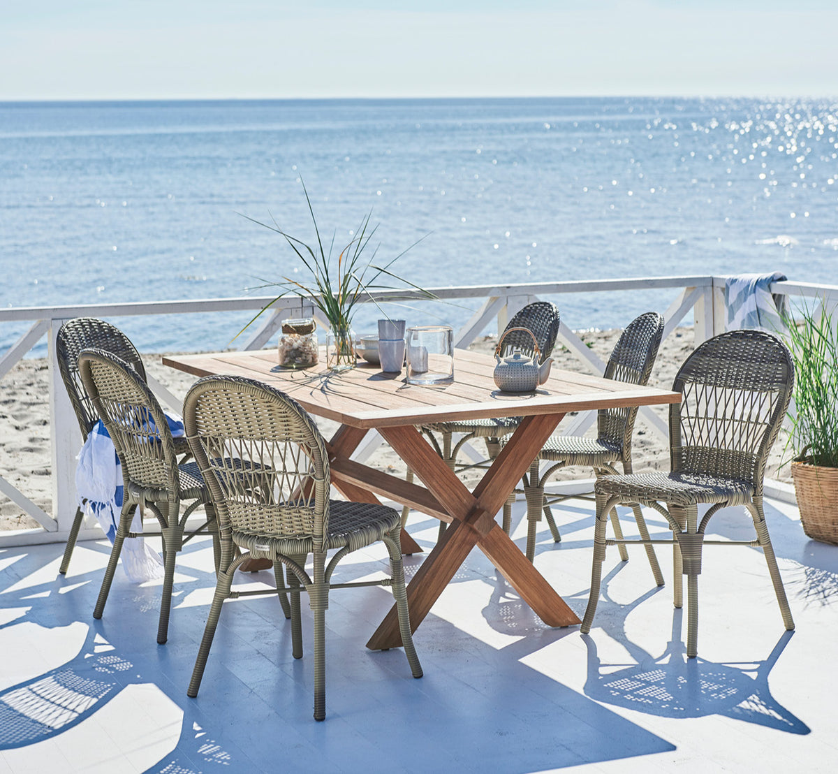 Dette er et livsstilsbillede af Colonial Bord 160 i outdoor Teak, på en strandterrasse med hvidt trædæk og havudsigt.