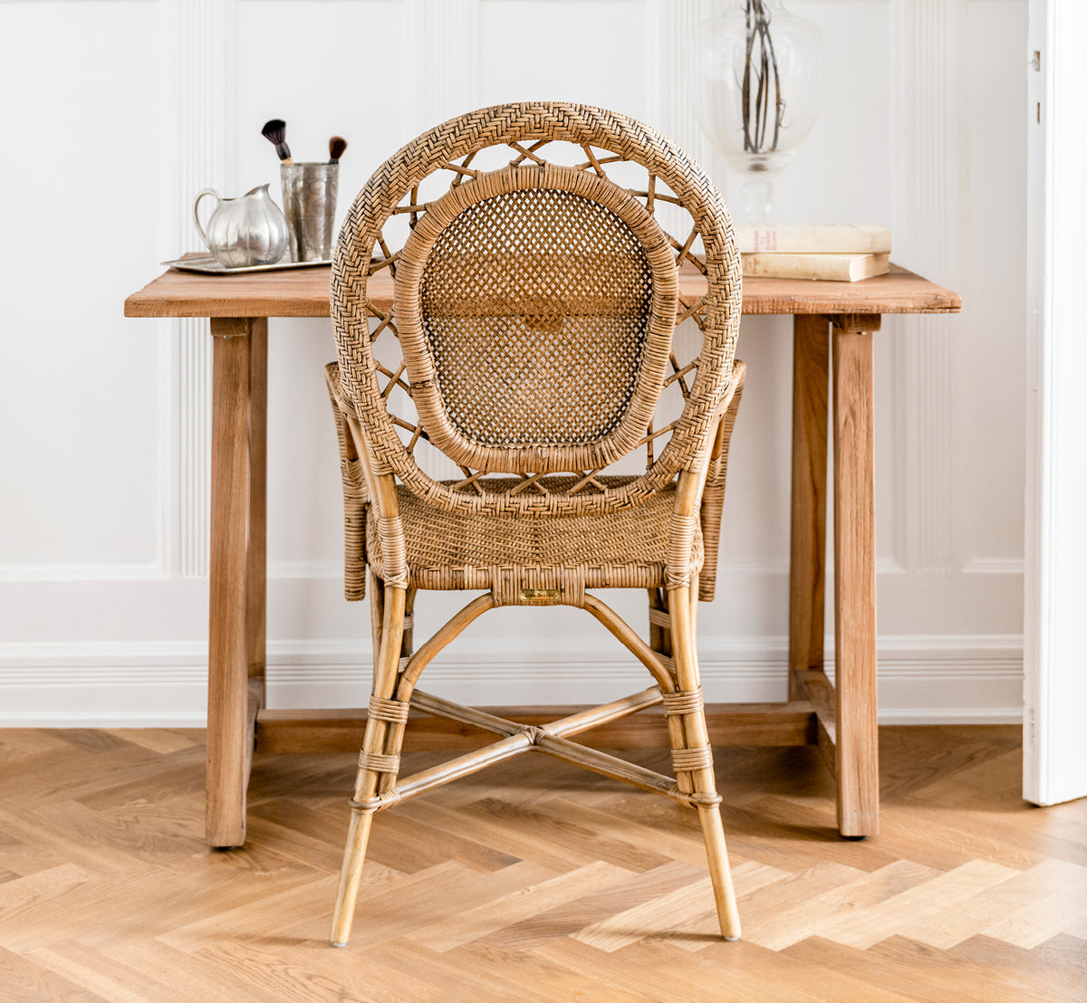 Dette er et livsstilsbillede af Lucas Teak Skrivebord i teak indoor. Placeret mod en grå væg med et teakspejl og pampasgræs i en entré.