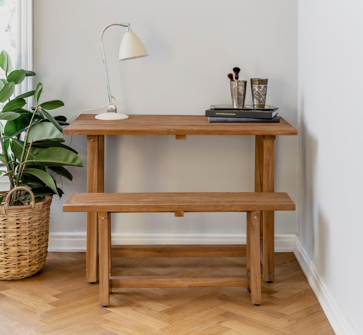 Dette er et livsstilsbillede af Lucas Teak Skrivebord i teak indoor. Stylet med en matchende bænk, skrivebordslampe og bøger i et hyggeligt hjørne.