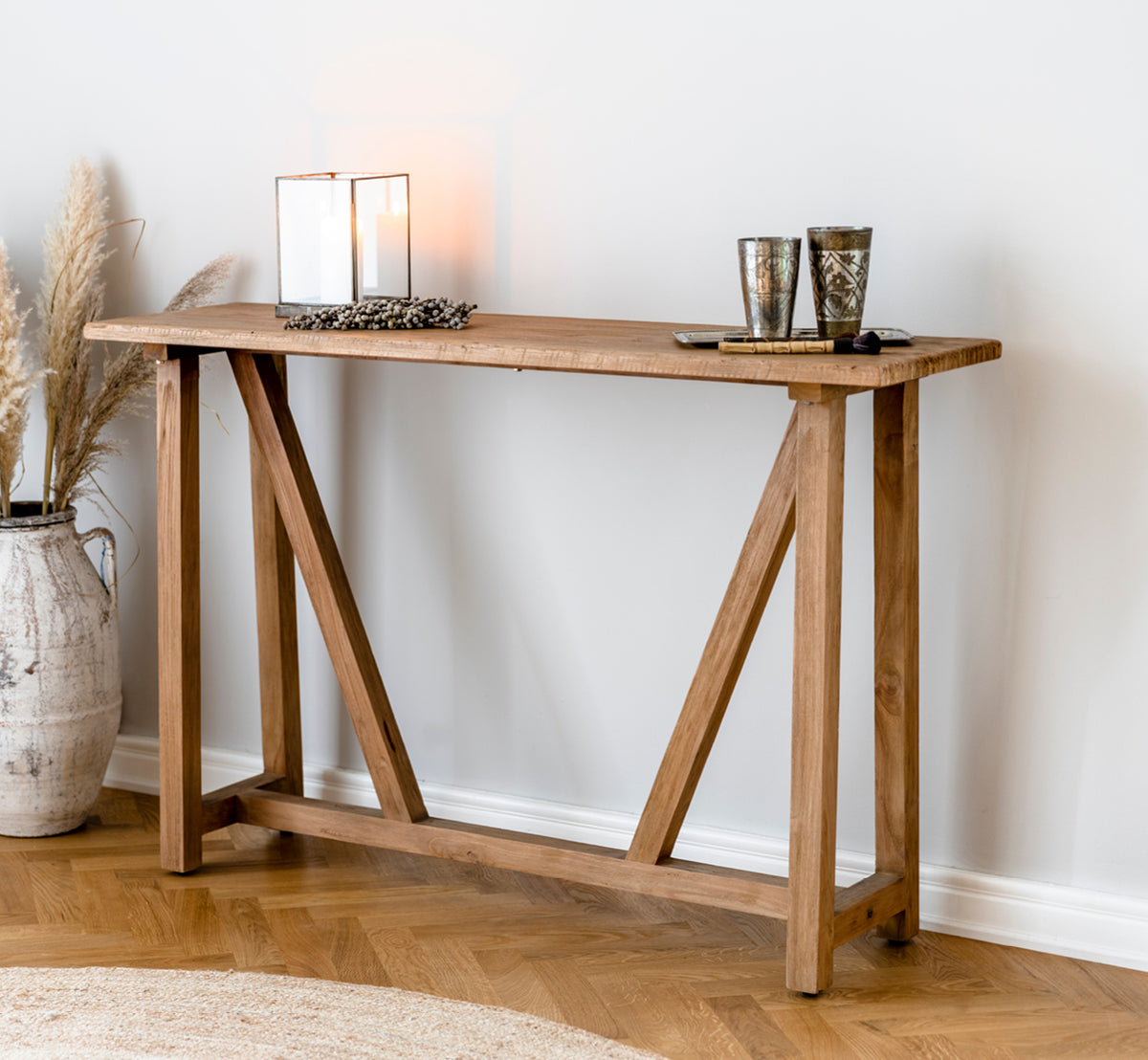 Dette er et livsstilsbillede af Lucas Teak Konsol i teak indoor. Stylet med lysestager og pampasgræs i et varmt miljø med et jutetæppe.