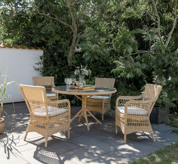Dette er et livsstilsbillede af Grace Udendørs spisebord i natural ArtFibre Aluminium, på en frodig haveterrasse med stengulv og overhengende træer.