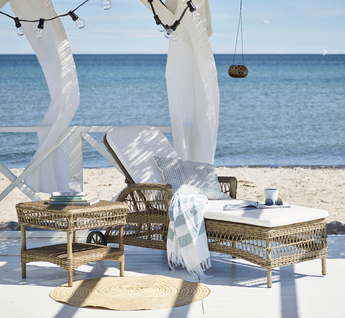 Dette er et livsstilsbillede af Susy Sidebord i antique Grey ArtFibre Aluminium, på en kystterrasse med havudsigt, strandgræs og hvide søjler.